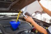 Car mechanic replacing and pouring fresh oil into engine at maintenance repair service station